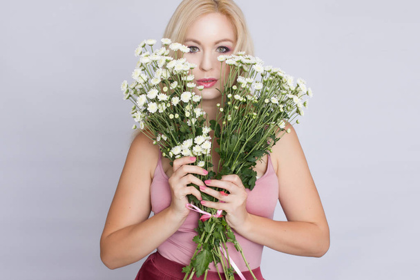 Portrait of a happy blonde woman in pink attire holding a bouquet of white wildflowers in hands - Photo, Image