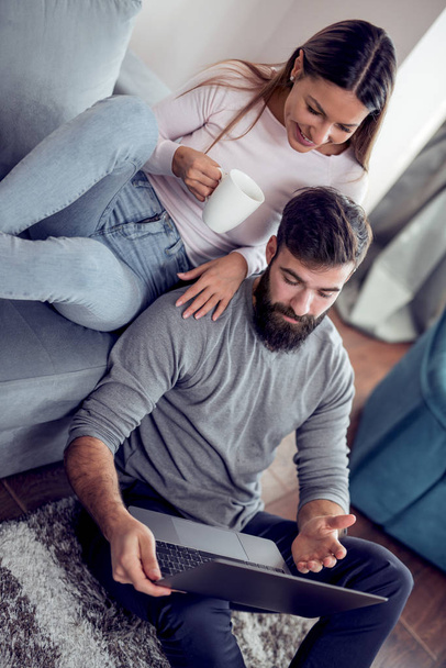 Jeune couple se détendre sur le canapé avec ordinateur portable dans leur salon à la maison
. - Photo, image