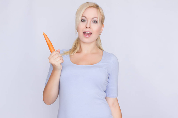 Happy blonde woman holding a carrot in her han - Foto, Bild