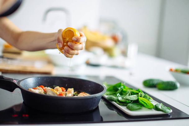 Young housewife cooking in kitchen, squeezing the orange on the frying pan - Fotoğraf, Görsel