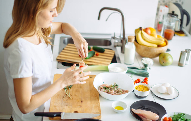 Woman making kebabs from meat and vegetable on chopping board in kitchen - Foto, Bild