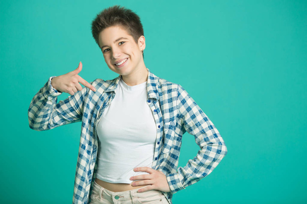 beautiful young girl with short hair in a shirt on a blue background pointing with her finger - Фото, изображение