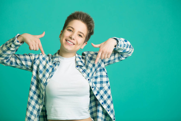 beautiful young girl with short hair in a shirt on a blue background pointing with her finger - Foto, imagen