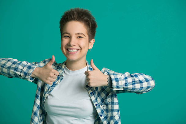 beautiful young girl with short hair in a shirt on a blue background pointing with her finger - Foto, Imagen