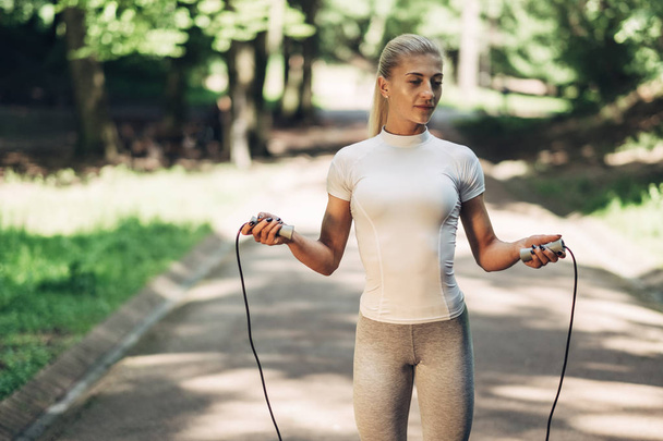 Portrait of Fit Young Woman with Jump Rope in Park. Fitness Female Doing Workout Outdoors in Park on Sunny Day. - Foto, Bild