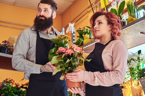 zwei Floristinnen, eine schöne rothaarige Frau und ein bärtiger Mann in Uniform, die im Blumenladen arbeiten. - Foto, Bild