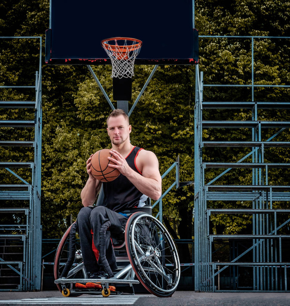 Σακάτεμα μπασκετμπολίστας σε μια αναπηρική καρέκλα κατέχει μια μπάλα σε μια ανοικτή gaming έδαφος. - Φωτογραφία, εικόνα