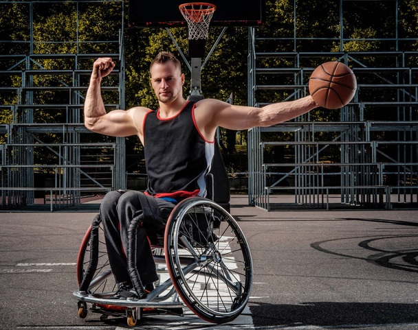 Сильний баскетболіст у позі інвалідного візка з м'ячем на відкритому ігровому майданчику
. - Фото, зображення