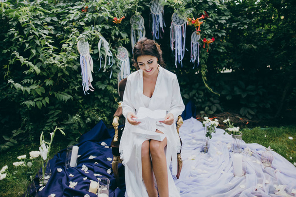 Beautiful  bride in the morning in garden reading letter - Foto, afbeelding