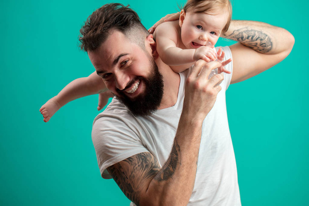 Playful father carrying his smiling infant child on neck over blue background - Foto, Bild