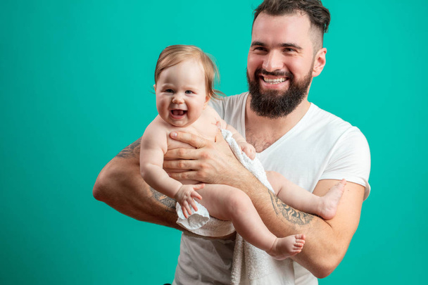 Playful father carrying his smiling infant child on neck over blue background - Фото, изображение