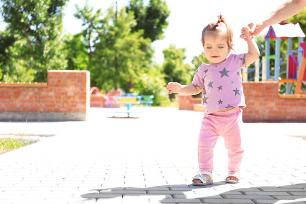 Adorable niña sosteniendo la mano de la madre mientras aprende a caminar al aire libre
 - Foto, imagen