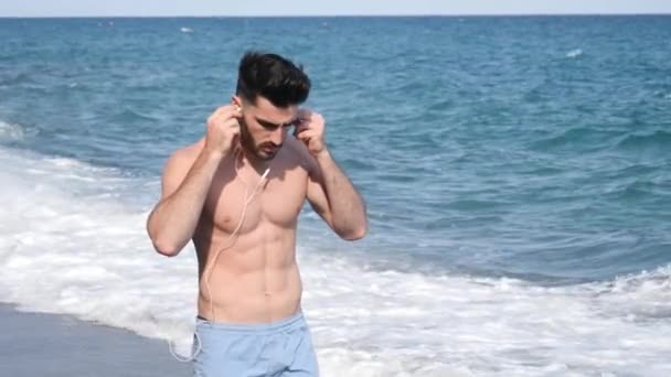 Young man at beach listening to music with earphones - Séquence, vidéo