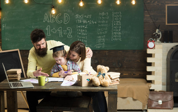 Homeschooling concept. Parents teaches son, chalkboard on background. Boy listening to mom and dad with attention. Parents teaching kid, speaking. Family cares about education of their son - Foto, afbeelding