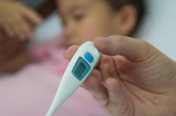 A sick girl with her mother measures fever with a digital thermometer. - Fotografie, Obrázek