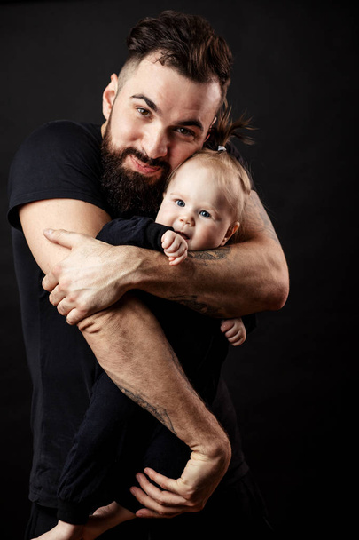 Young athletic father with adorable baby on black background - Foto, Imagem
