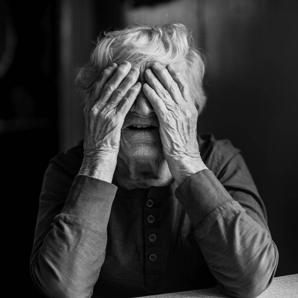 Μια ηλικιωμένη γυναίκα καλύπτει το πρόσωπό της με ζαρωμένα χέρια. Μαύρο και άσπρο φωτογραφία. - Φωτογραφία, εικόνα