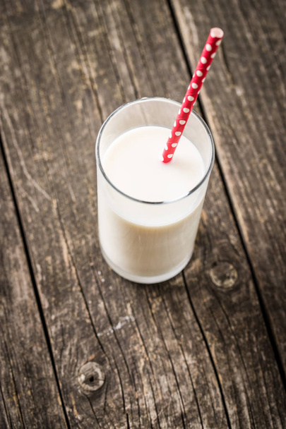 Glass of milk and red straw on old wooden table. - Photo, image