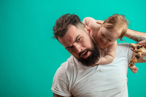 Playful father carrying his smiling infant child on neck over blue background - Photo, Image