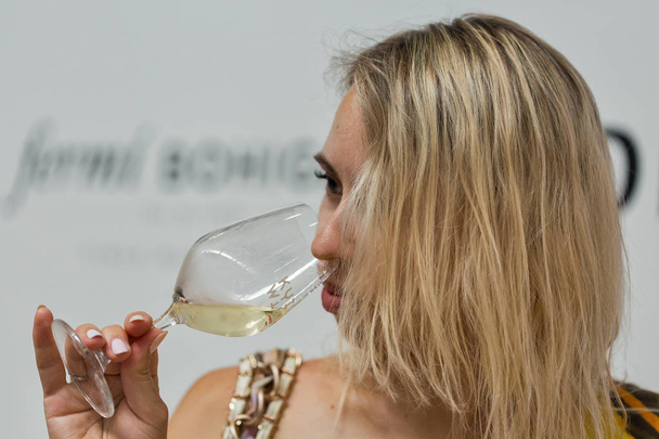 КИЕВ, УКРАИНА - 2 июня 2018 года: Молодая женщина пробует белое вино на Киевском винном фестивале. Большой фестиваль вина и продуктов питания был организован компанией Good Wine, в нем приняли участие 77 виноделов со всего мира
. - Фото, изображение