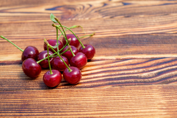 Molte ciliegie rosse mature sul tavolo di legno su aria aperta. Vista da vicino. Copia spazio per testo
. - Foto, immagini