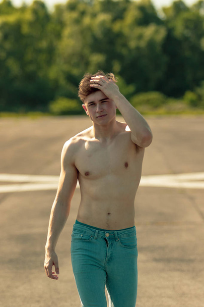 Young adult male walking forward shirtless while running a hand through his hair, on a warm summer's day - Фото, зображення