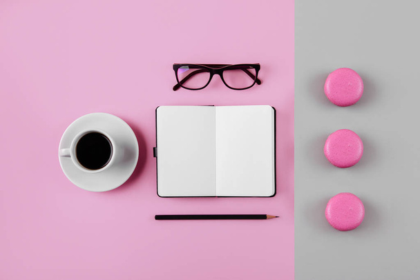 Coffee, macaron, clean notebook, eyeglasses and flower on pink table from above. Female working desk. Flat lay style. - Fotoğraf, Görsel