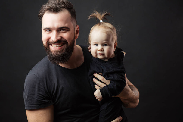 Young athletic father with adorable baby on black background - Photo, image