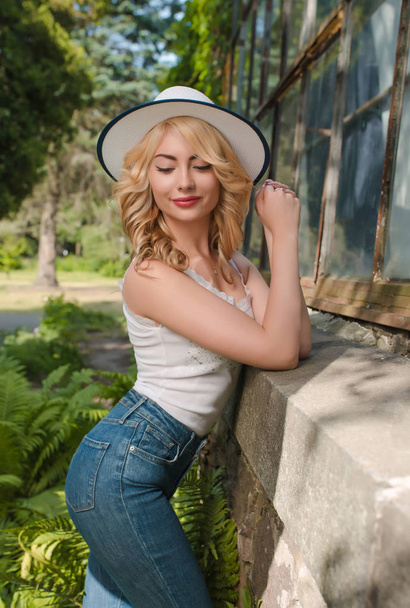 Cool mujer rubia con sombrero y ropa elegante posando cerca del invernadero
 - Foto, Imagen