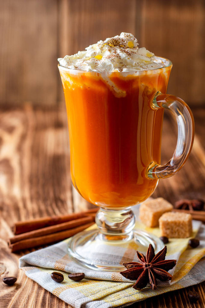Pumpkin spice latte with whipped cream and cinnamon in glass on rustic wooden background. Selective focus. - 写真・画像