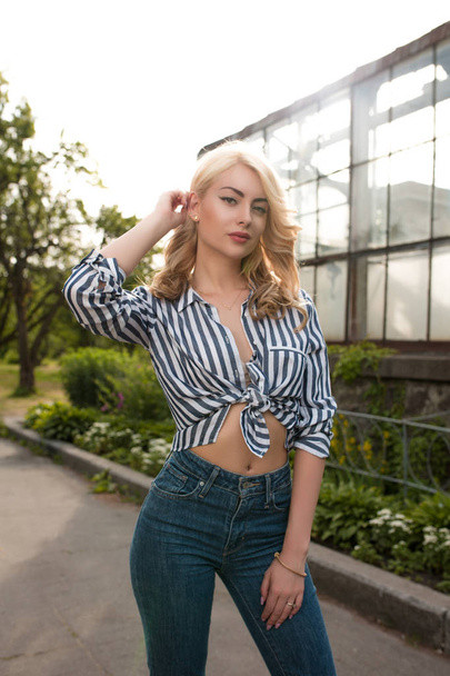 Elegant young model wearing striped shirt, blue jeans and posing with sun glare - Фото, зображення