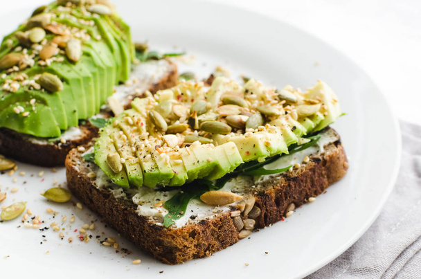 Healthy avocado toasts for breakfast or lunch with rye bread, sliced avocado, arugula, pumpkin and sesame seeds, salt and pepper. Vegetarian sandwiches. Plant-based diet. Whole food concept. - Photo, Image