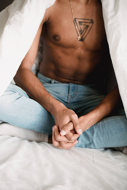 Portrait of handsome african black man sitting in bed with Crossed fingers in fist . Contrast black and white - Фото, изображение