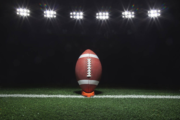 A football on a tee on a yard line under lights at night - Foto, imagen