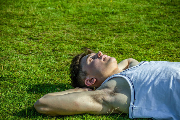 A young adult male sunbathing, laying on short grass on a warm summer's day - 写真・画像