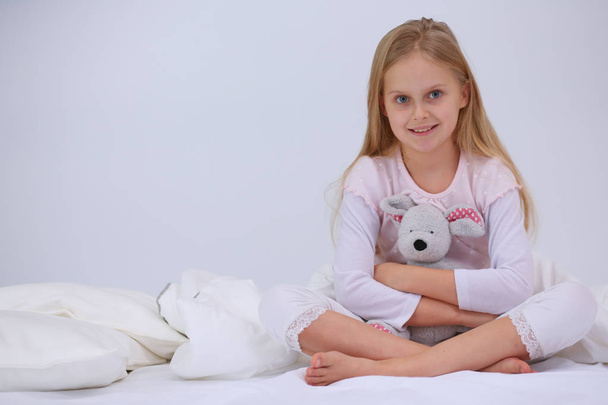 Pieni tyttö makuuhuoneessa istuu sängyllä. Pikkutytöllä on pyjama päällä ja hän istuu sängyssä.
 . - Valokuva, kuva