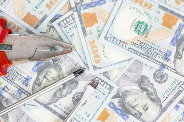 Tools lying over 100 dollars banknotes background. Pliers and screwdriver against US money. Correction, fixing and improvement of budget concept. Copyspace. - Photo, Image