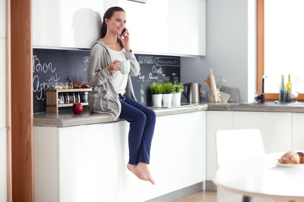nő ül a modern konyha mobiltelefon használata. - Fotó, kép