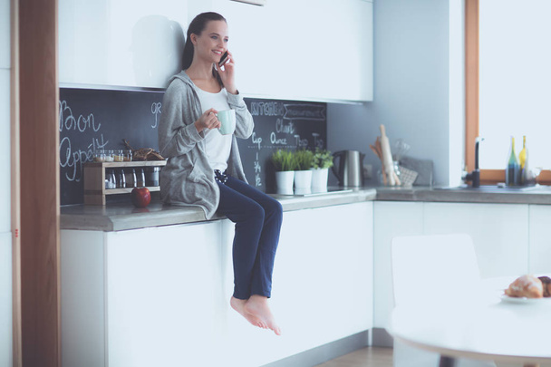 Woman using mobile phone sitting in modern kitchen. - Photo, Image