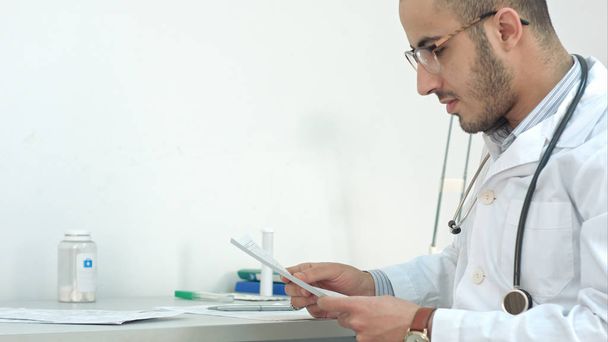 Young doctor in glasses showing medical results to his patient - Фото, изображение