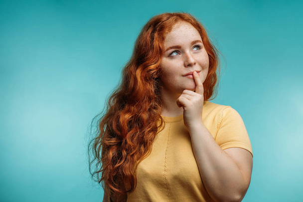 Cute cheerful redhead young girl in yellow over blue background with face. - 写真・画像