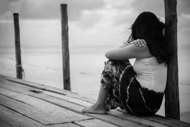 Μαύρο και άσπρο του ΕΔΕ και μοναχική γυναίκα που κάθεται μόνη μια η ξύλινη γέφυρα πάνω από την θάλασσα - Φωτογραφία, εικόνα