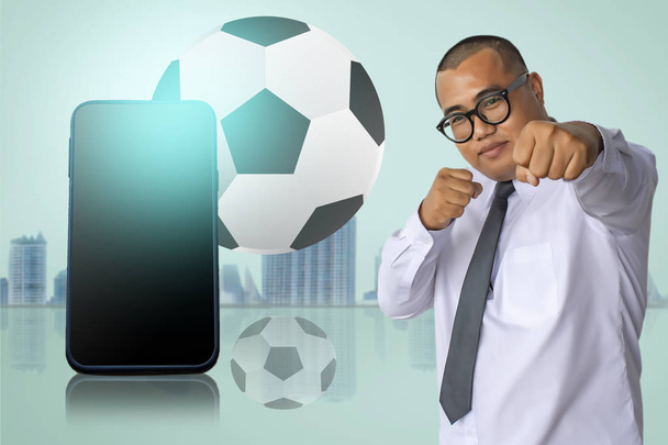 Asian business man punching with smart phone on city blurry background with football tournament 2018 - Photo, Image