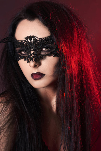 mooi meisje op halloween in mask.young vrouw in het masker. rood gekleurde spots portret - Foto, afbeelding