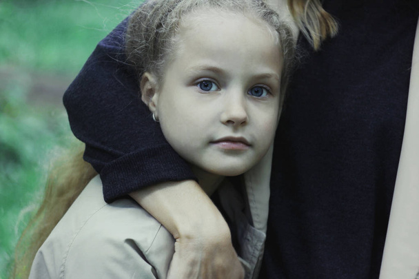 Dziewczyna lat 7 z niebieskimi oczami, patrząc na kamery, przytulanie jej matka - Zdjęcie, obraz