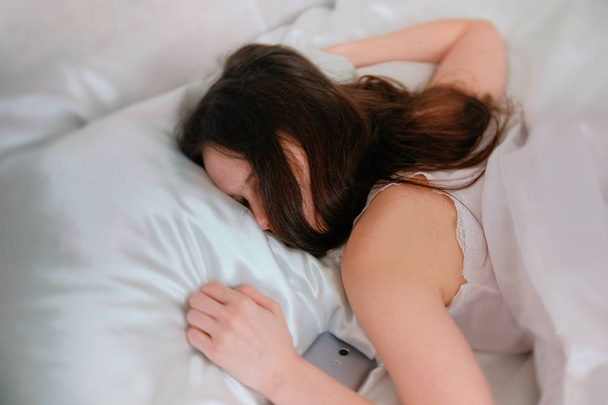 Young woman brunette sleeping in bed. Mobile phone near her. - Foto, Imagen