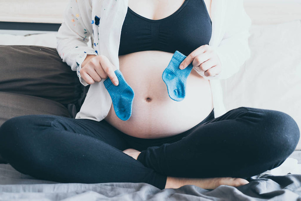 Ventre de la femme enceinte avec les mains en choisissant des chaussettes pour bébé - point de mise au point sélectif avec style de filtre vintage
 - Photo, image
