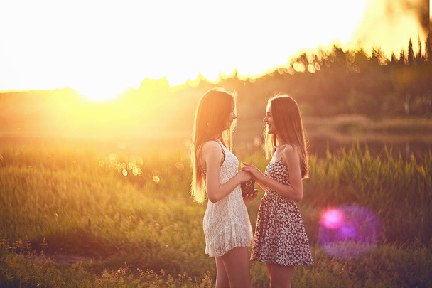 Jonge meisjes permanent op gras in de zonnestralen en hand in hand. - Foto, afbeelding