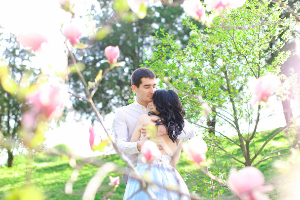 Jong meisje en brunette man knuffelen in de buurt van bloeiende boom. - Foto, afbeelding