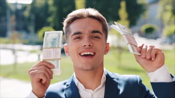 Happy young businessman holding a big amount of money in his hands. He stands in the street near the office center or bank. Business style, winnings, deposit, success, career - Кадри, відео